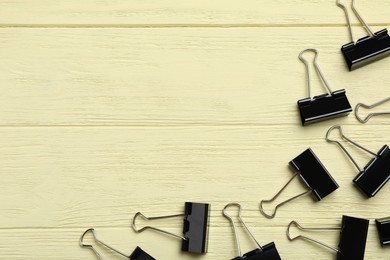 Photo of Black binder clips on yellow wooden table, flat lay. Space for text