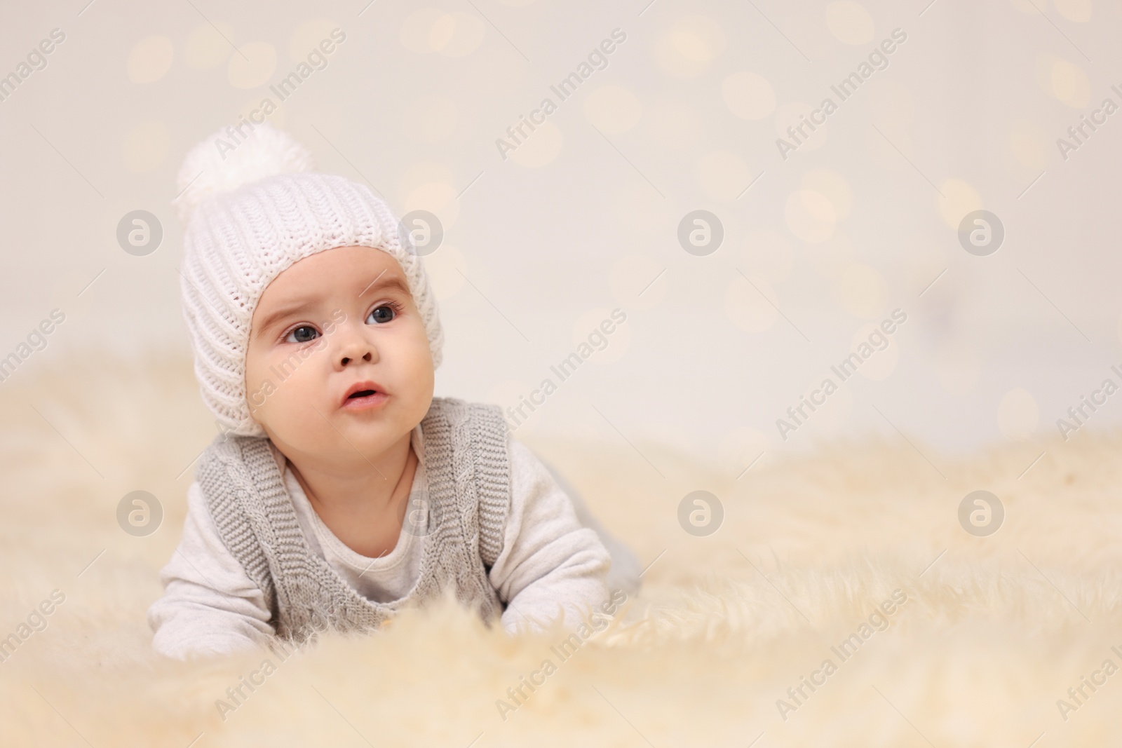 Photo of Cute baby on fluffy carpet against blurred festive lights, space for text. Winter holiday