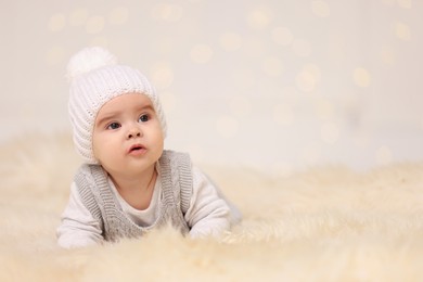 Photo of Cute baby on fluffy carpet against blurred festive lights, space for text. Winter holiday