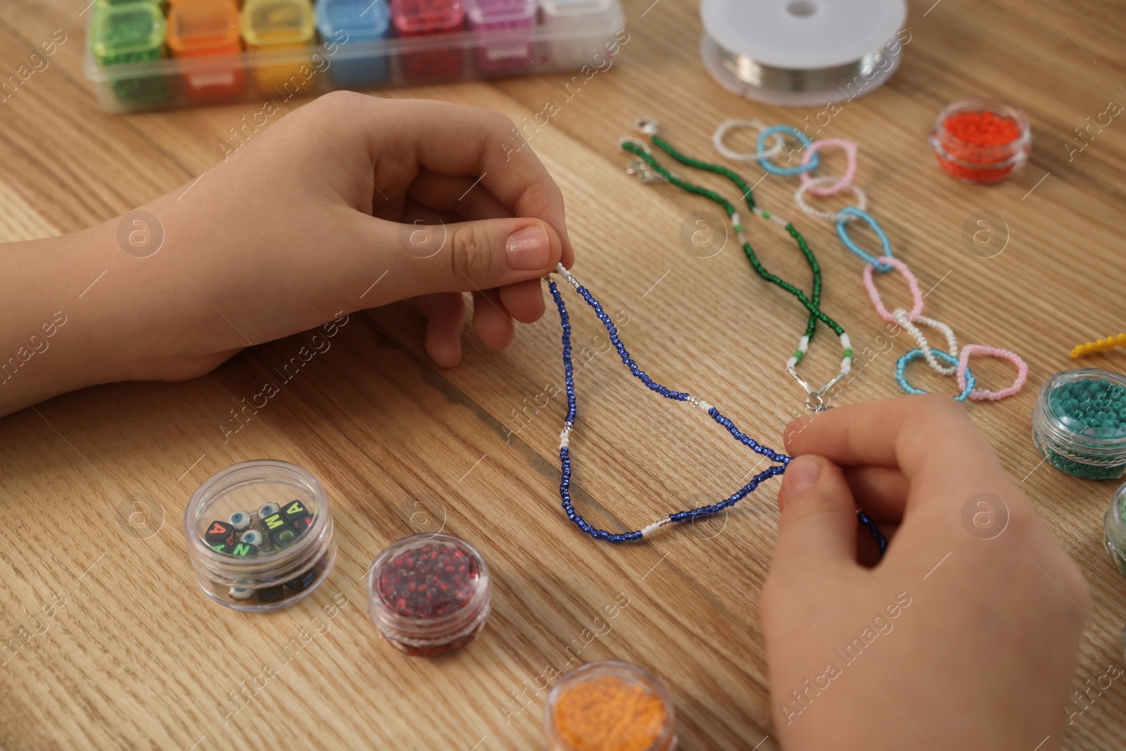 Photo of Girl making beaded jewelry at wooden table, closeup