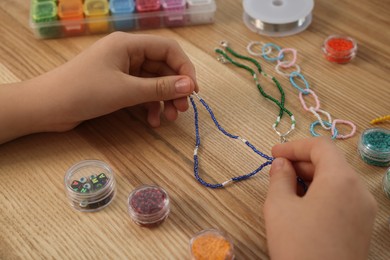 Photo of Girl making beaded jewelry at wooden table, closeup