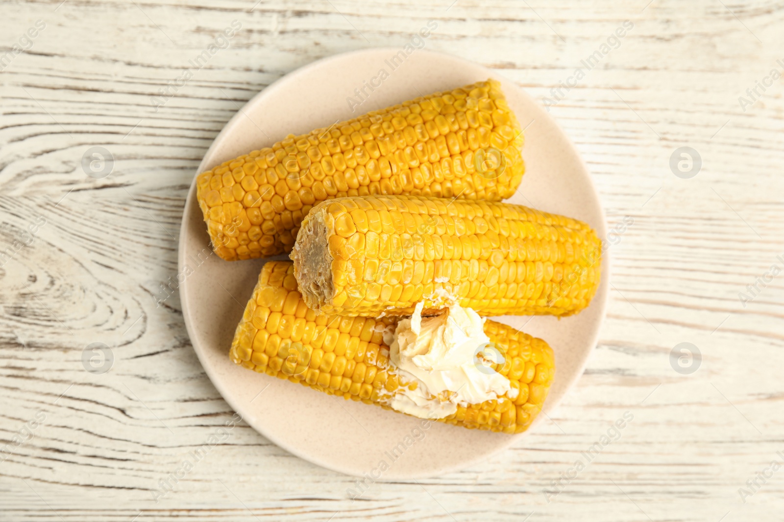 Photo of Delicious boiled corn with butter on white wooden table, top view