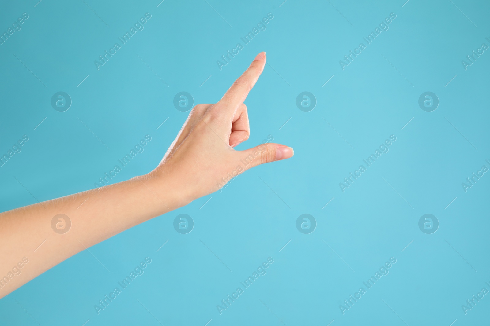 Photo of Woman pointing at something on light blue background, closeup. Finger gesture