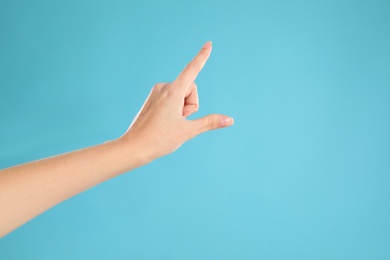 Woman pointing at something on light blue background, closeup. Finger gesture