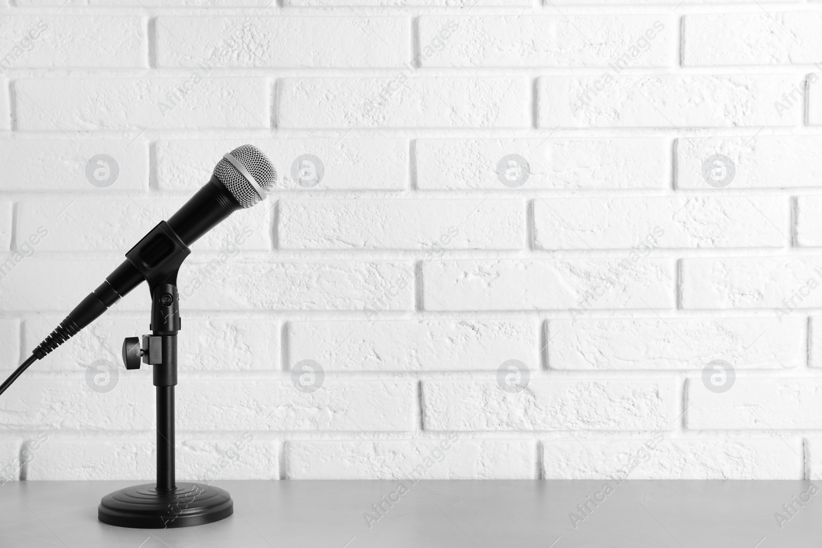 Photo of Modern microphone on table near brick wall. Space for text