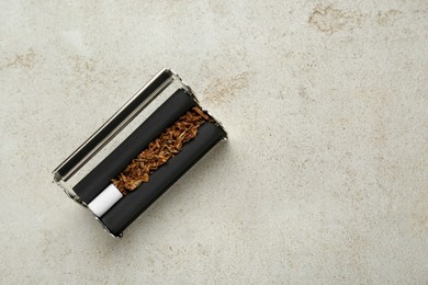 Photo of Roller with tobacco and filter on light grey table, top view and space for text. Making hand rolled cigarettes