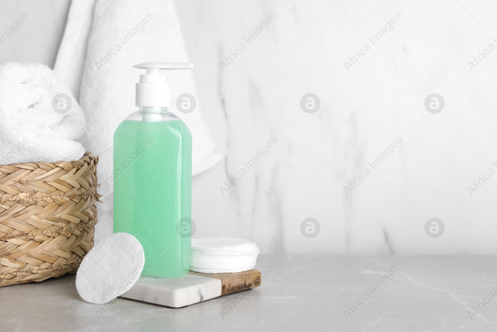 Photo of Bottle of face cleansing product, cotton pads and towel on light grey table. Space for text