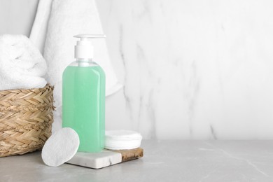 Photo of Bottle of face cleansing product, cotton pads and towel on light grey table. Space for text