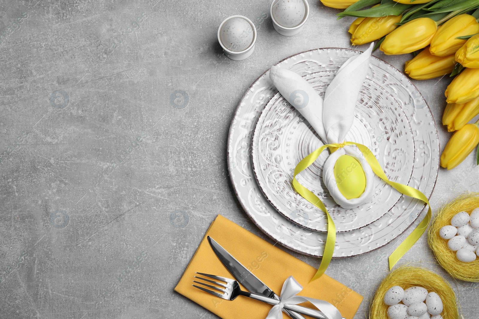 Photo of Festive table setting with bunny made of painted egg and napkin on light grey background, flat lay with space for text. Easter celebration