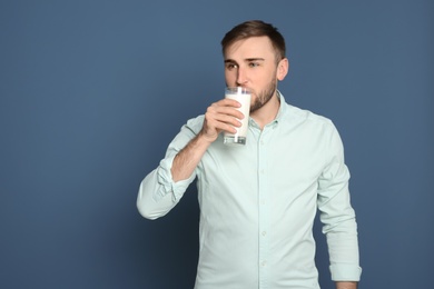 Young man drinking tasty milk on color background