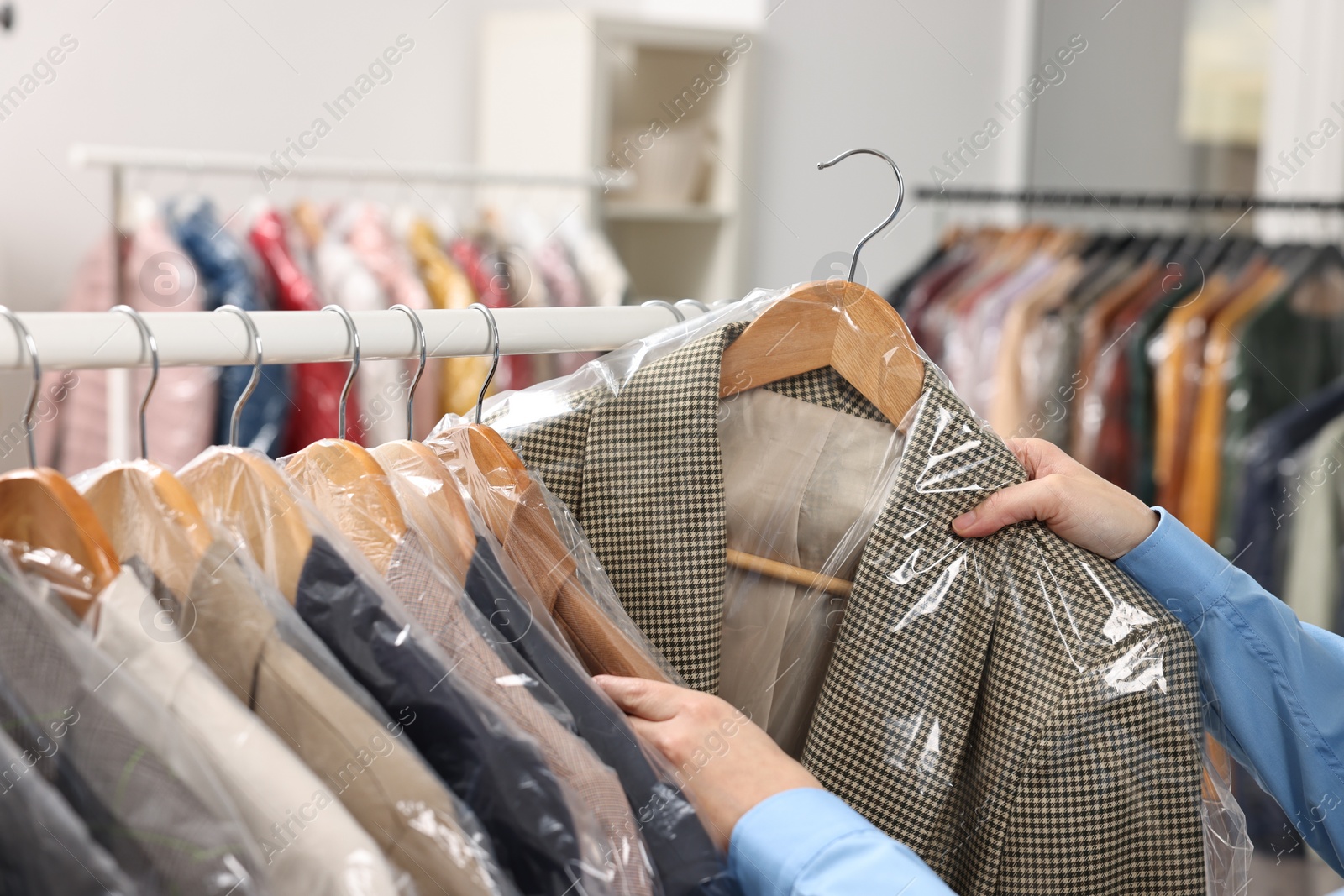 Photo of Dry-cleaning service. Woman taking jacket in plastic bag from rack indoors, closeup