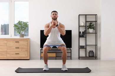 Athletic man doing exercise with elastic resistance band on mat at home