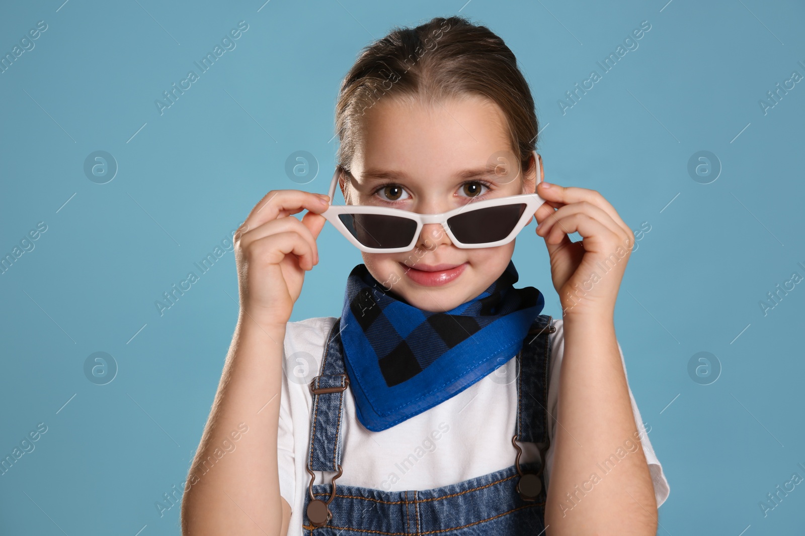 Photo of Cute little girl wearing stylish bandana and sunglasses on turquoise background