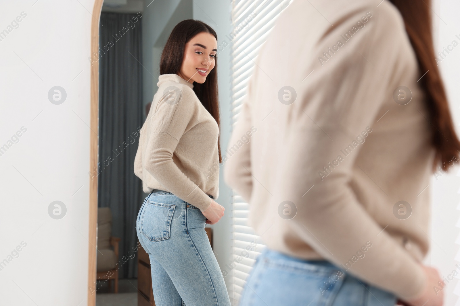 Photo of Young woman in stylish jeans near mirror indoors