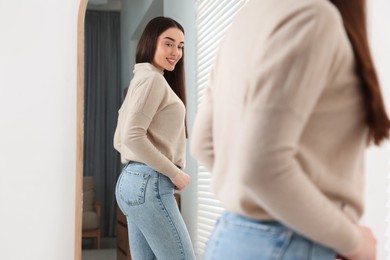 Photo of Young woman in stylish jeans near mirror indoors