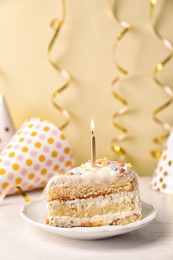 Slice of delicious birthday cake with candle on table