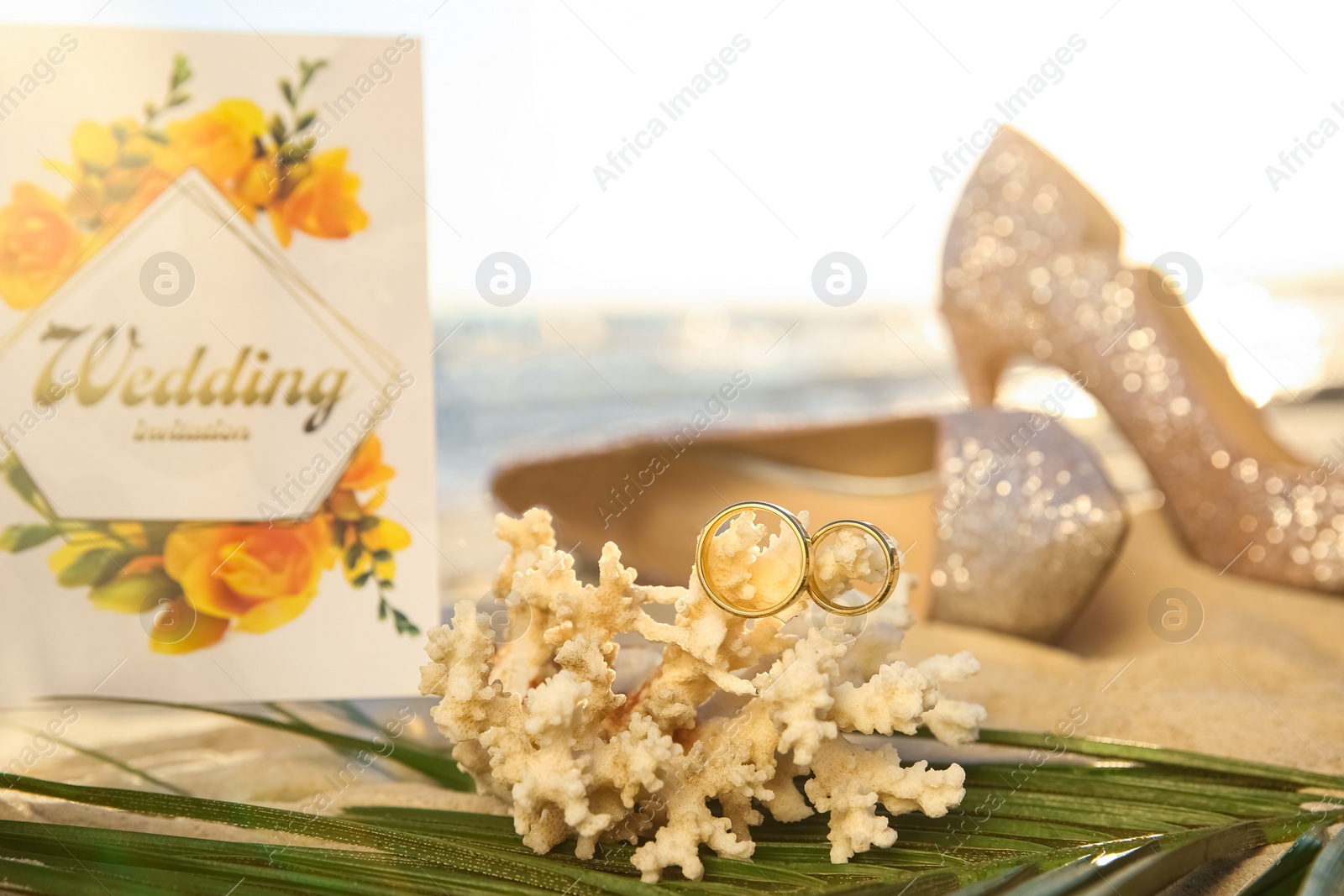 Photo of Coral with gold rings and wedding invitation on sandy beach