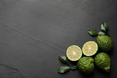 Photo of Fresh ripe bergamot fruits with green leaves on black table, flat lay. Space for text