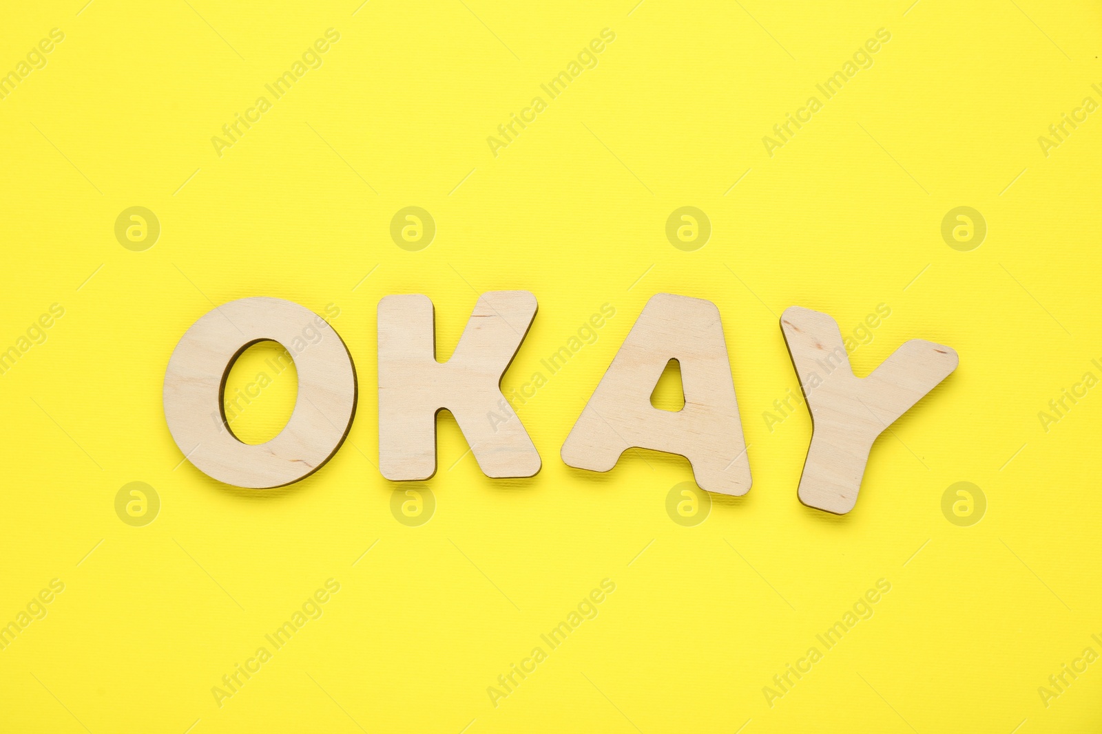 Photo of Word Okay made of wooden letters on yellow background, top view