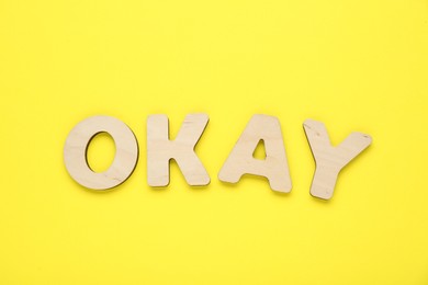 Word Okay made of wooden letters on yellow background, top view