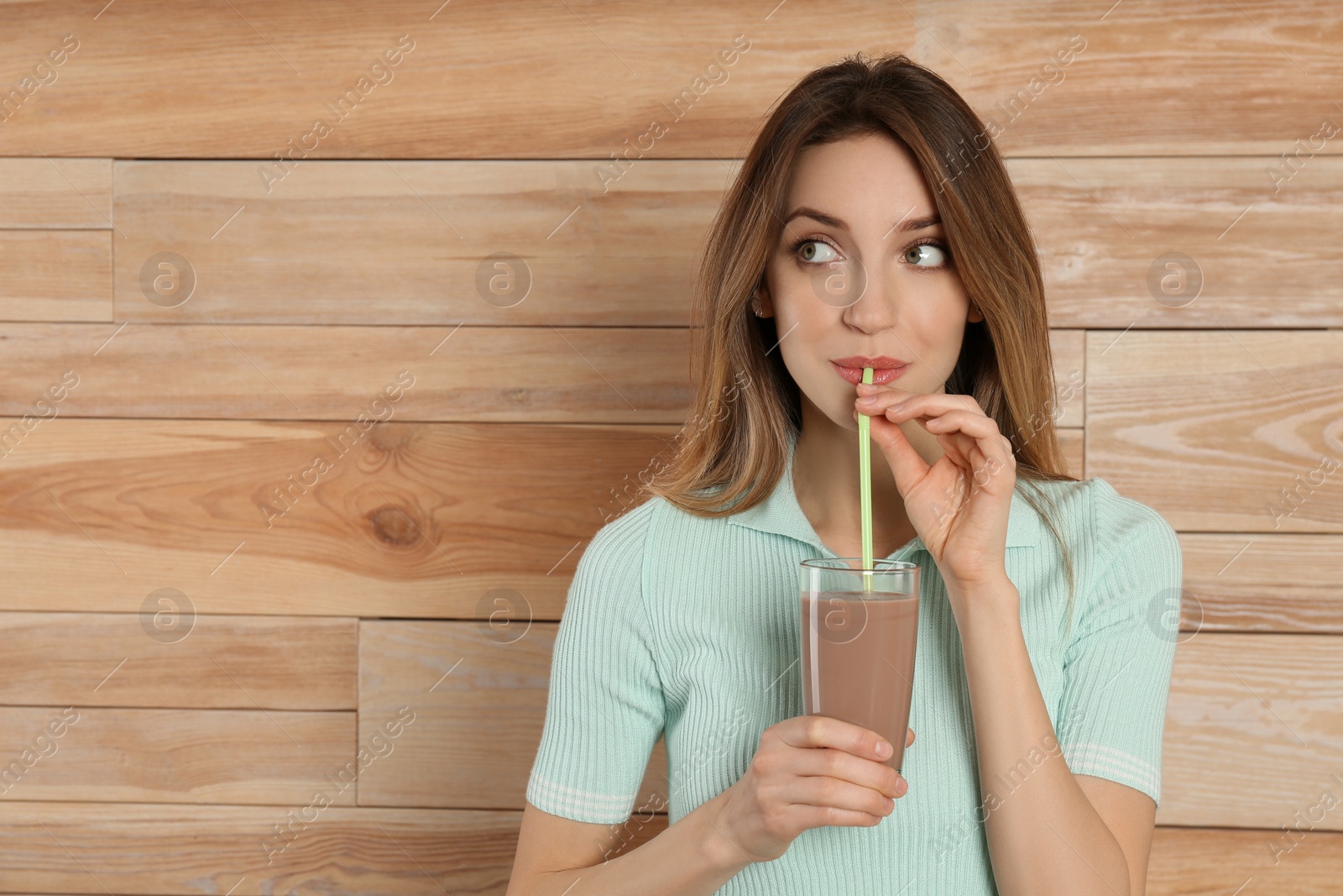Photo of Young woman drinking chocolate milk on wooden background. Space for text