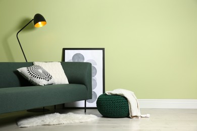 Stylish living room interior with comfortable knitted pouf and sofa near light green wall, space for text
