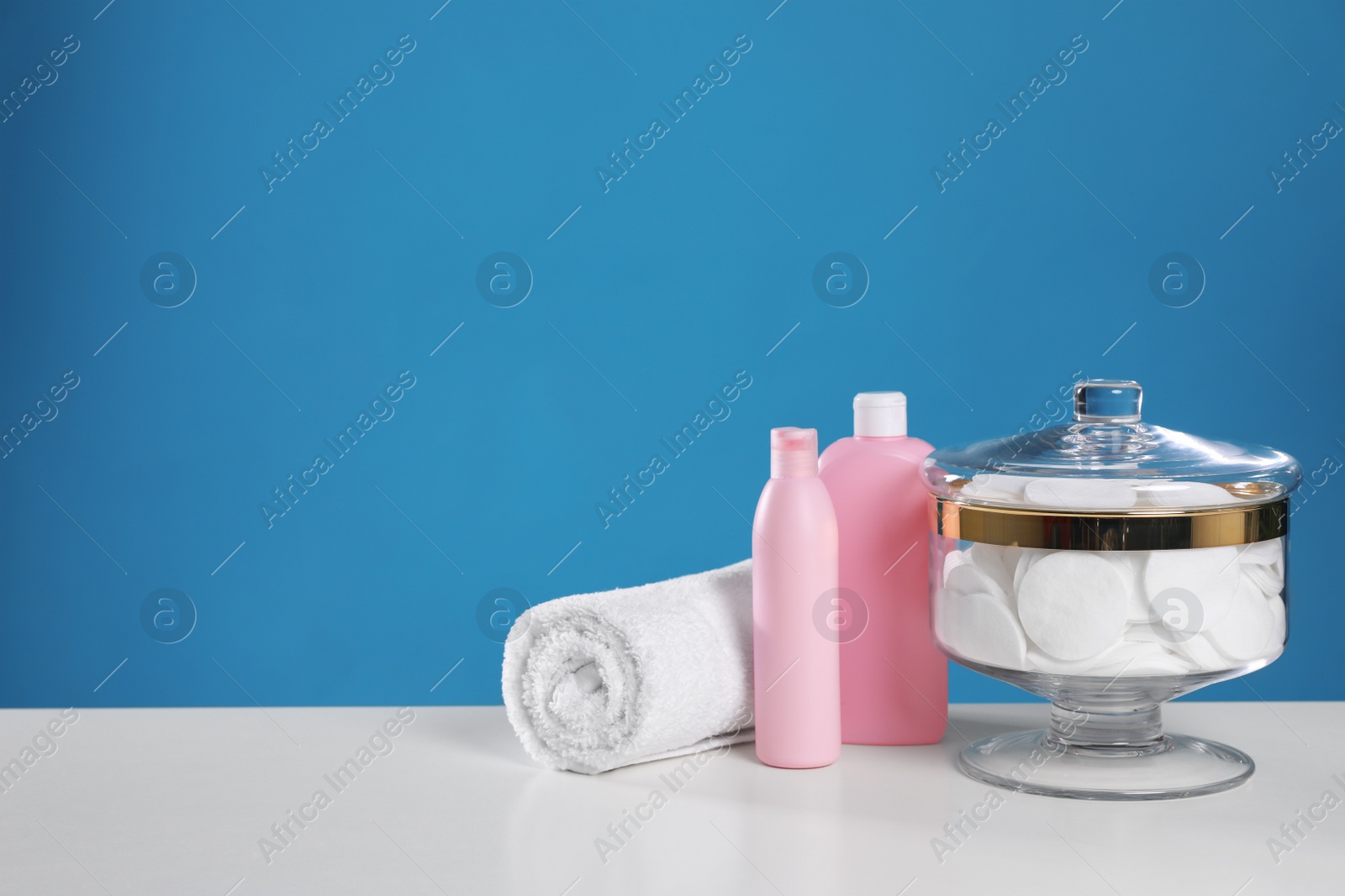 Photo of Jar with cotton pads on white table against blue background. Space for text