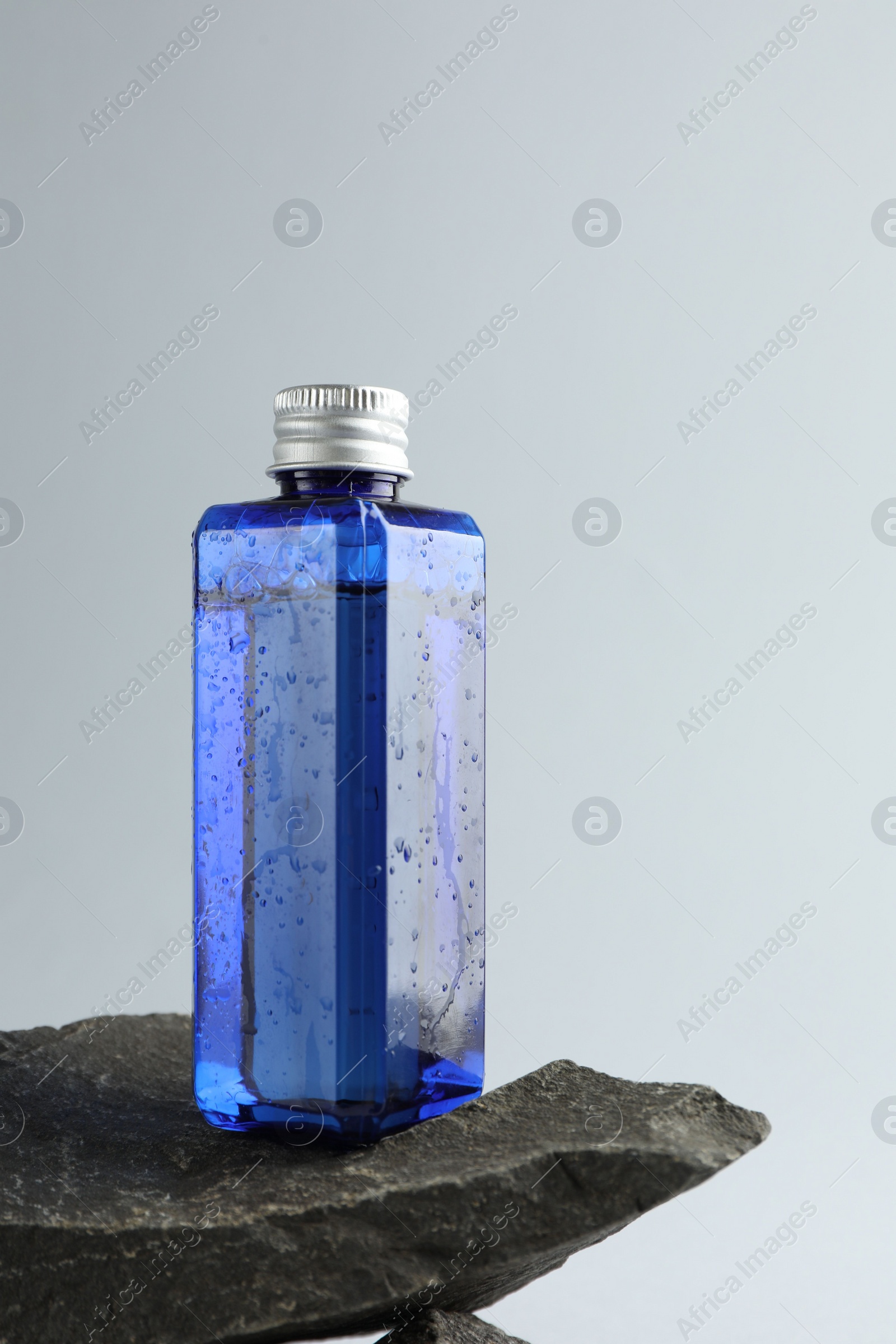 Photo of Bottle of cosmetic product on stone against light grey background, space for text