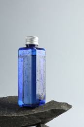 Bottle of cosmetic product on stone against light grey background, space for text