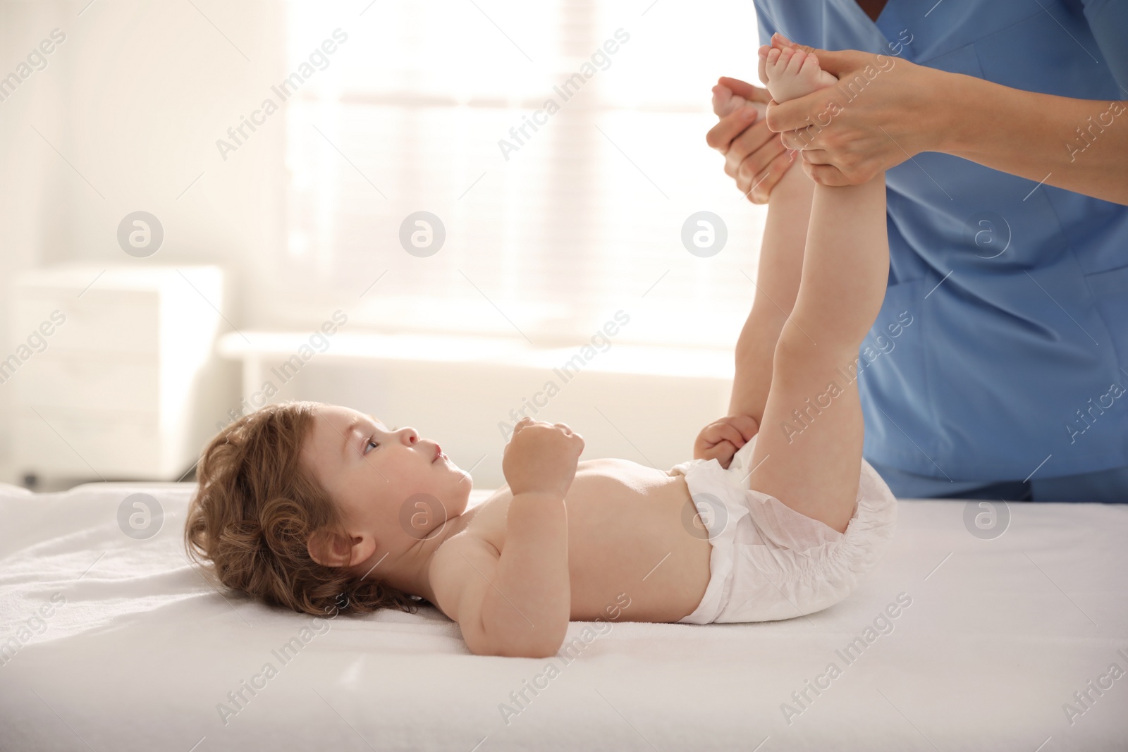 Photo of Orthopedist examining little baby on bed indoors