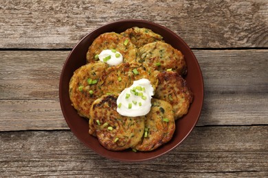 Photo of Delicious zucchini pancakes with sour cream and green onion on wooden table, top view