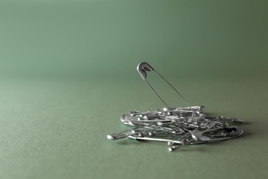 Photo of Pile of safety pins on green background, space for text