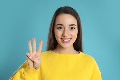 Woman showing number three with her hand on light blue background