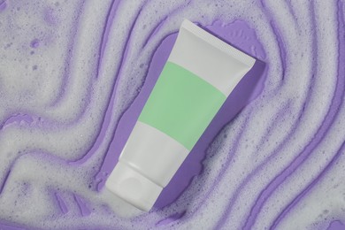 Tube with cleansing foam on violet background, top view. Cosmetic product