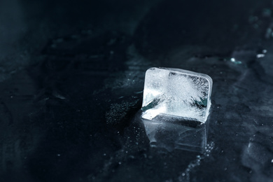 Photo of Ice cube on wet black surface, closeup. Space for text