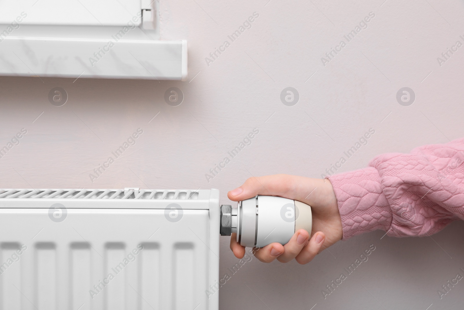 Photo of Girl adjusting heating radiator thermostat near white wall indoors, closeup