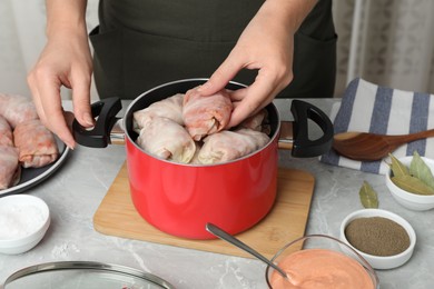 Woman putting uncooked stuffed cabbage roll into pot at light grey marble table, closeup