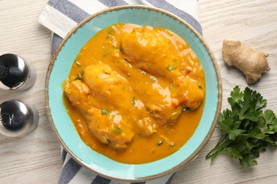 Tasty chicken curry, parsley and ginger on wooden table, flat lay