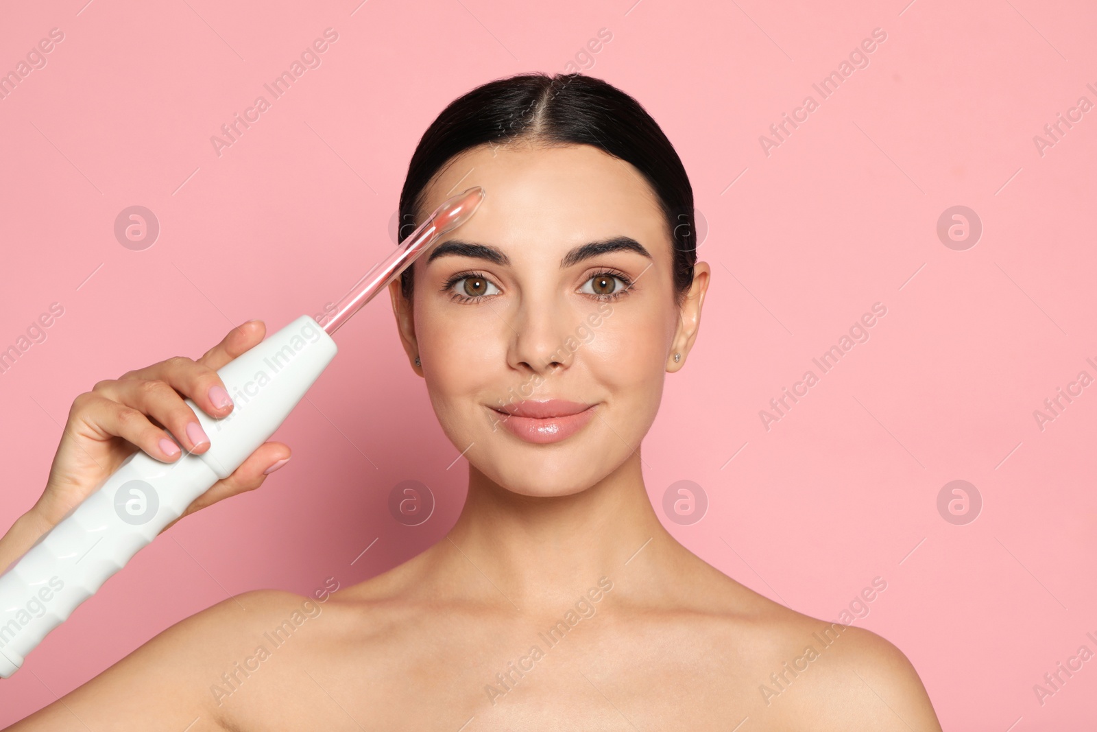 Photo of Woman using high frequency darsonval device on pink background. Space for text