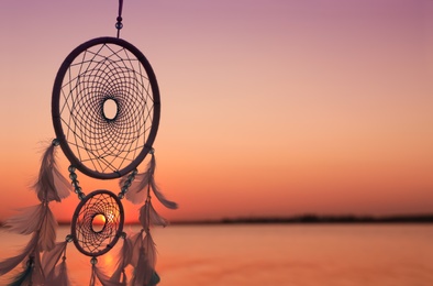 Photo of Beautiful handmade dream catcher near river at sunset. Space for text