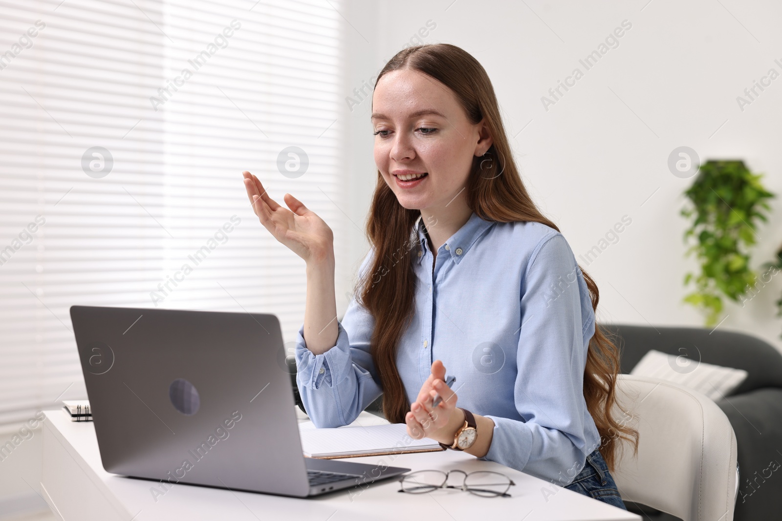 Photo of E-learning. Young woman using laptop during online lesson at white table indoors