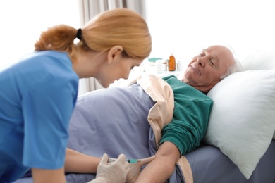 Nurse making injection to elderly man on bed indoors. Medical assistance