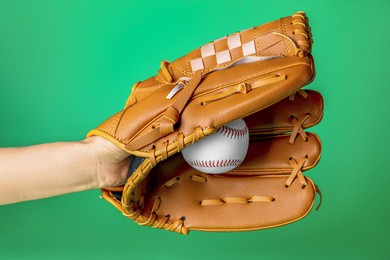Baseball player holding ball with catcher's mitt on green background, closeup. Sports game