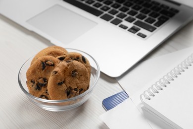 Bowl with chocolate chip cookies and laptop on white wooden table in office. Space for text