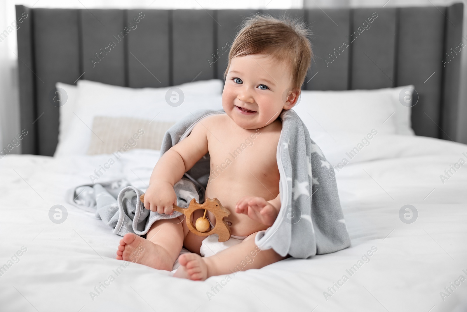 Photo of Happy baby boy with blanket and rattle sitting on bed at home