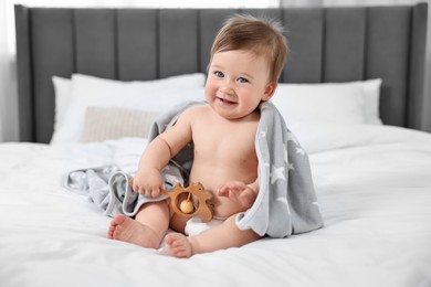 Photo of Happy baby boy with blanket and rattle sitting on bed at home
