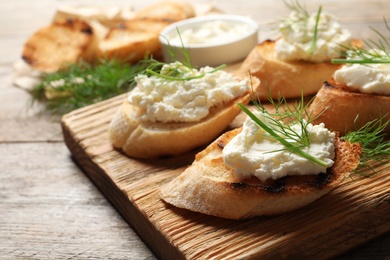 Toasted bread with tasty cream cheese on wooden board