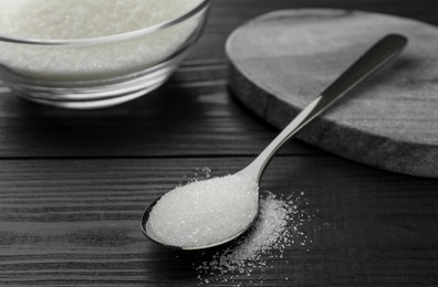 Photo of Spoon with granulated sugar on black wooden table, closeup