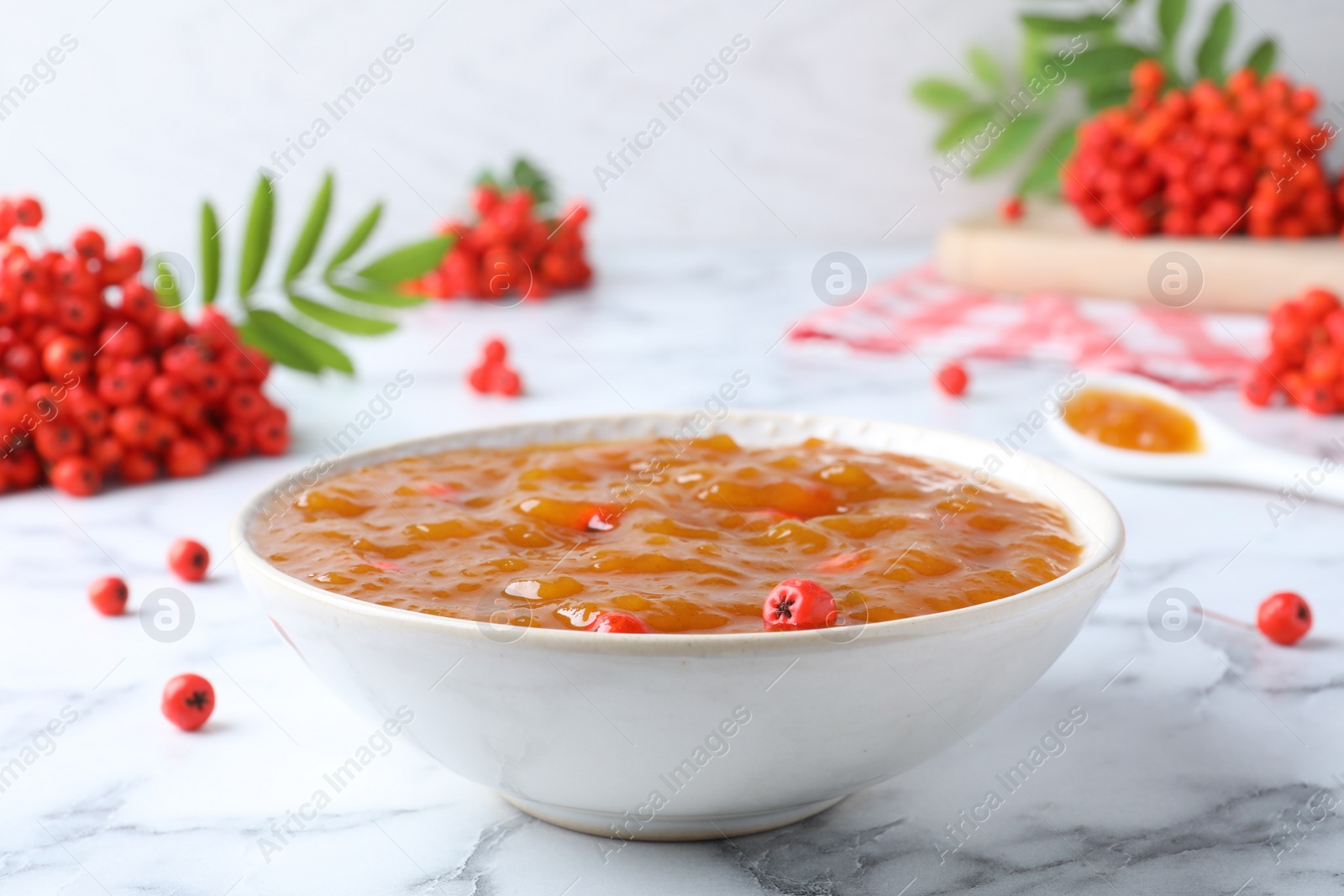 Photo of Delicious rowan jam in bowl and berries on white marble table, closeup