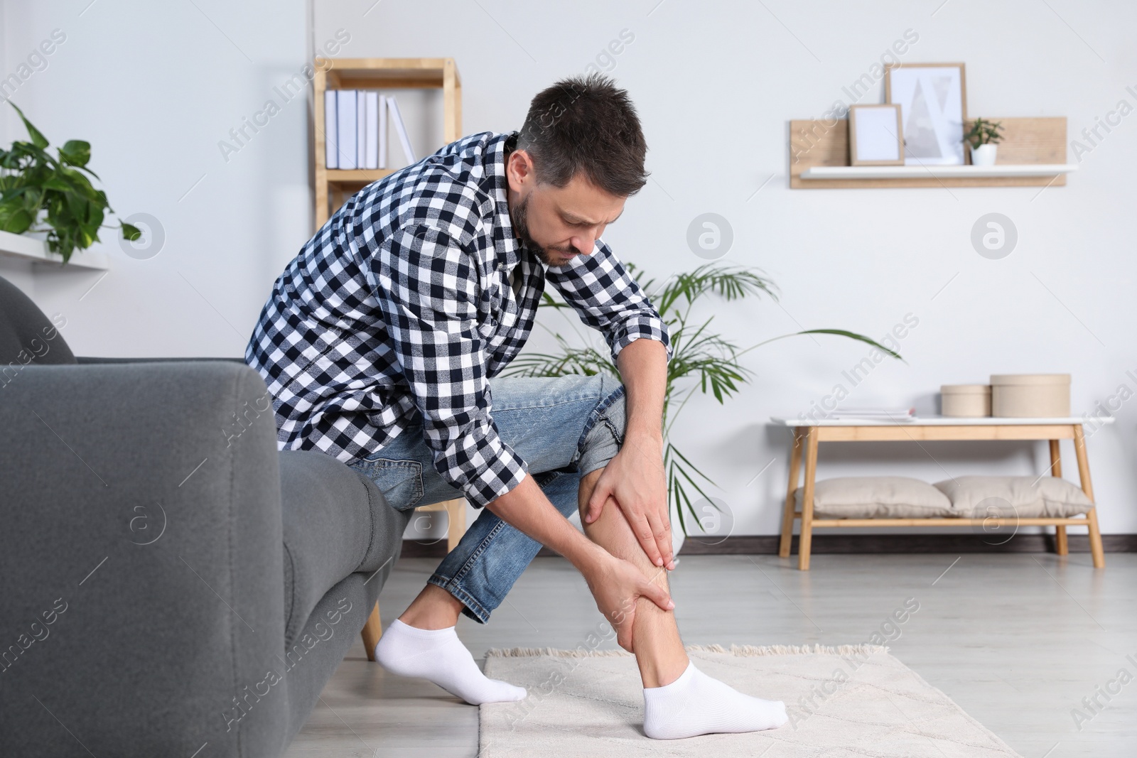 Photo of Man rubbing sore leg on sofa at home, space for text